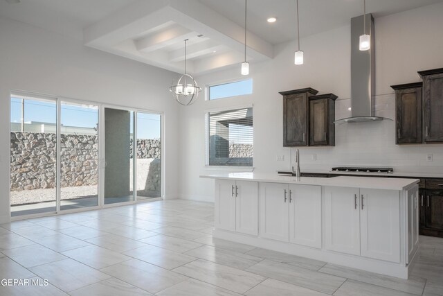 kitchen featuring decorative light fixtures, a center island with sink, plenty of natural light, and wall chimney range hood