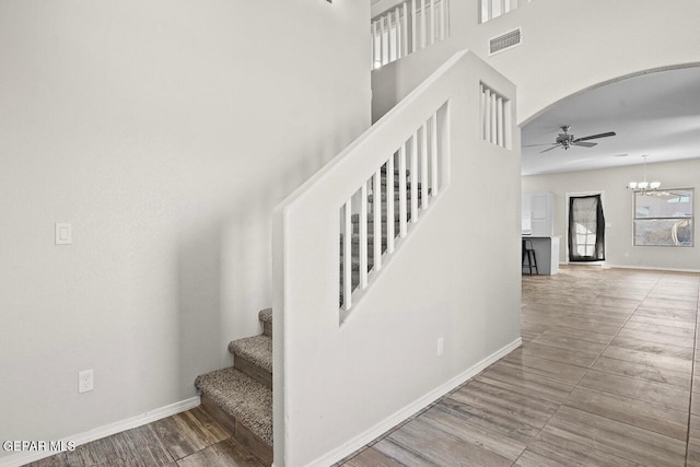 staircase with a towering ceiling, wood-type flooring, and ceiling fan with notable chandelier