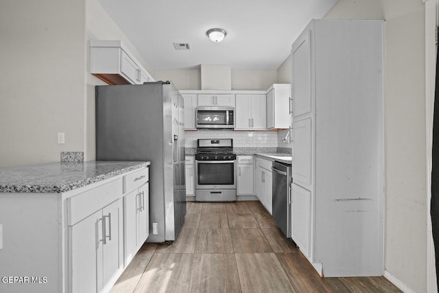 kitchen featuring sink, white cabinetry, tasteful backsplash, appliances with stainless steel finishes, and light stone countertops