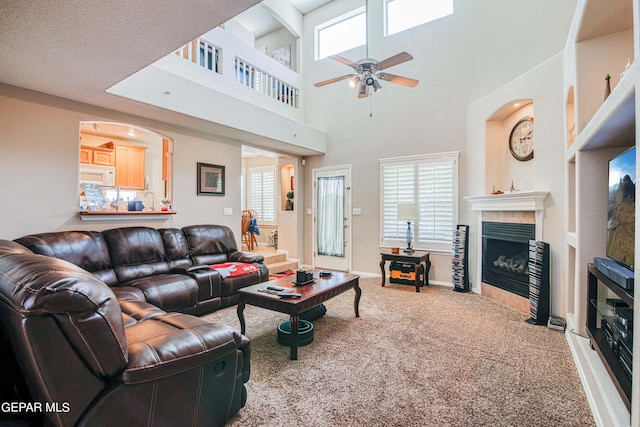 living room with a towering ceiling, ceiling fan, a textured ceiling, carpet flooring, and a fireplace