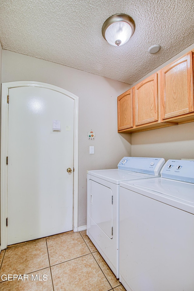 washroom featuring washer and clothes dryer, a textured ceiling, cabinets, and light tile floors