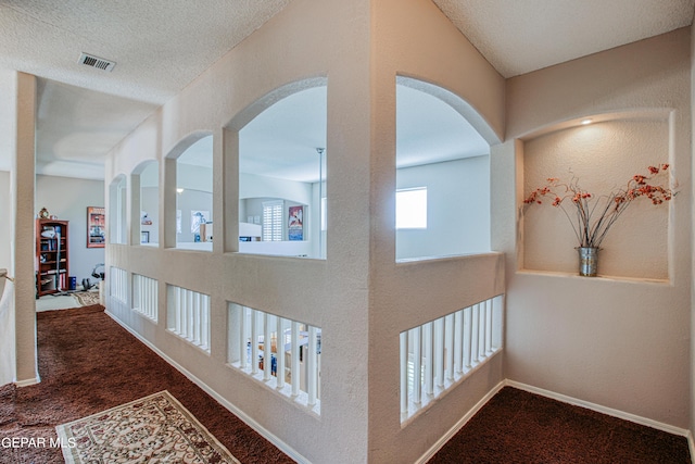 hallway featuring dark colored carpet and a textured ceiling