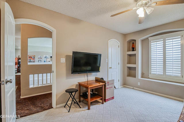 living room featuring light colored carpet, built in features, ceiling fan, and a textured ceiling