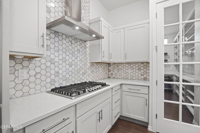 kitchen with white cabinets, dark hardwood / wood-style flooring, backsplash, wall chimney range hood, and stainless steel gas stovetop