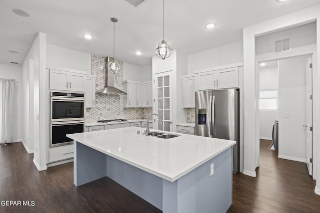 kitchen featuring backsplash, appliances with stainless steel finishes, dark wood-type flooring, wall chimney range hood, and sink