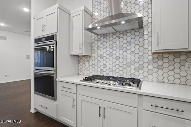 kitchen with wall chimney exhaust hood, white cabinets, dark hardwood / wood-style floors, backsplash, and appliances with stainless steel finishes