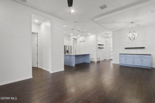 unfurnished living room featuring an inviting chandelier, dark hardwood / wood-style floors, and sink