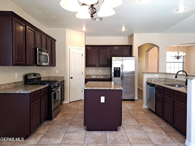 kitchen with light stone counters, a kitchen island, stainless steel appliances, sink, and light tile floors