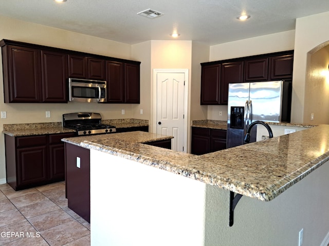 kitchen with light stone counters, appliances with stainless steel finishes, a center island, and light tile flooring