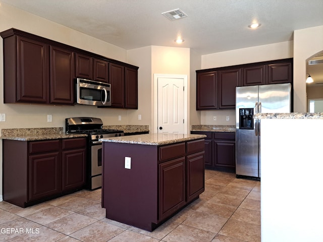 kitchen featuring light stone countertops, dark brown cabinetry, a kitchen island, light tile floors, and appliances with stainless steel finishes