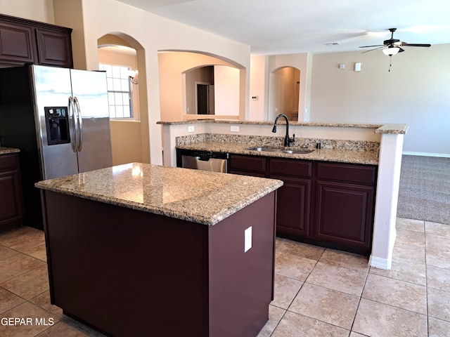 kitchen with light stone countertops, stainless steel appliances, a kitchen island, light colored carpet, and sink