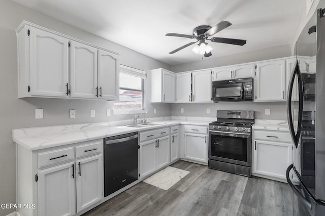 kitchen with white cabinets, light hardwood / wood-style flooring, black appliances, sink, and ceiling fan