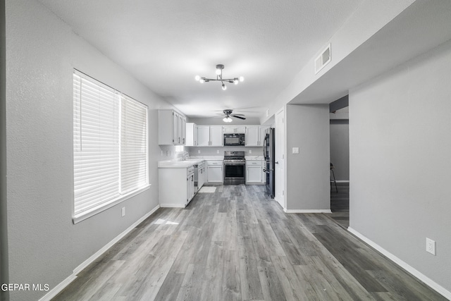 kitchen with hardwood / wood-style floors, ceiling fan with notable chandelier, white cabinets, and stainless steel appliances