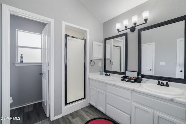 bathroom featuring wood-type flooring, a shower with shower door, double sink vanity, toilet, and lofted ceiling