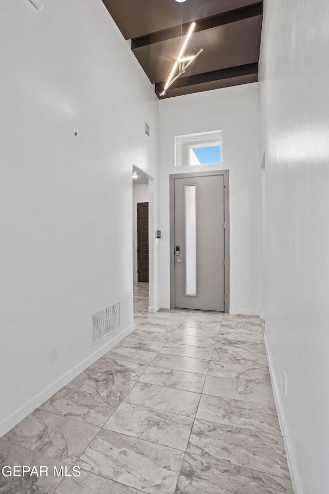 entryway with beamed ceiling, a high ceiling, and light tile floors