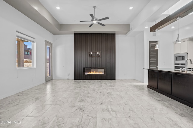 unfurnished living room with sink, ceiling fan, a large fireplace, and light tile floors