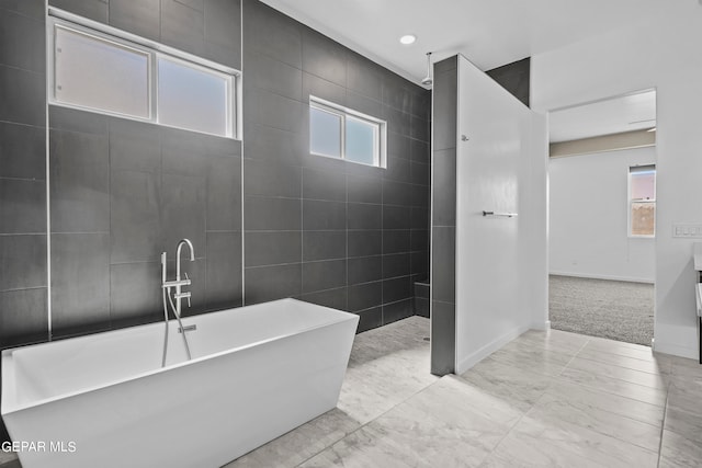 bathroom with a wealth of natural light, a bathing tub, tile flooring, and tile walls