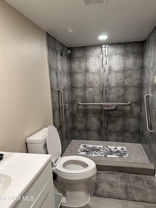 bathroom featuring a tile shower, vanity, and toilet