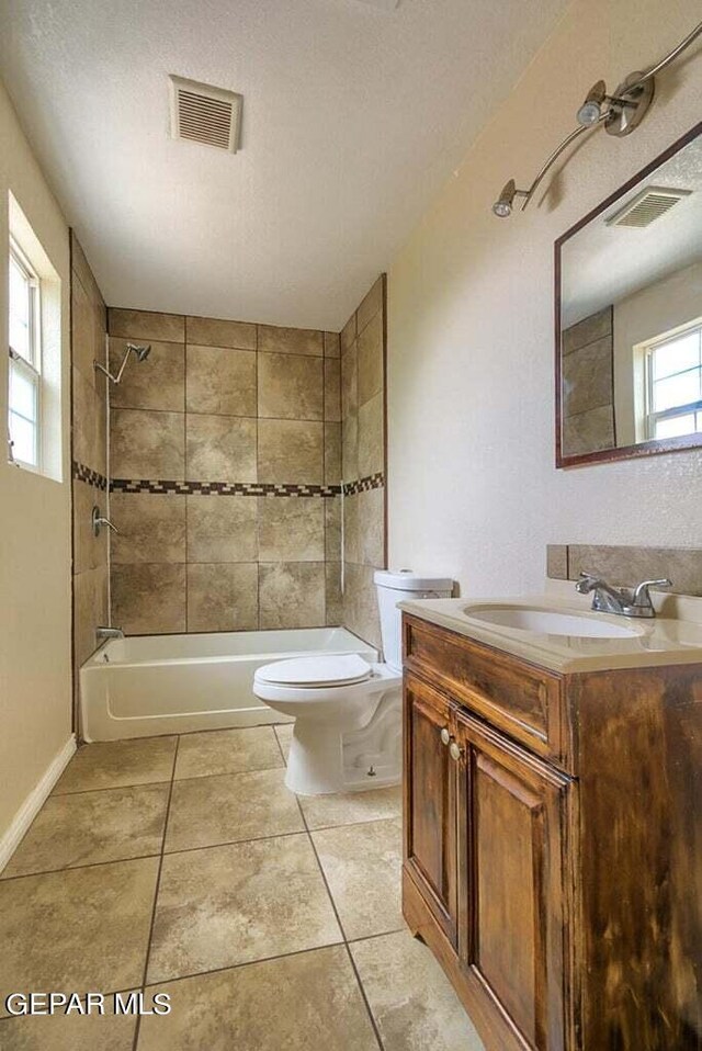 full bathroom featuring tiled shower / bath combo, a textured ceiling, tile floors, toilet, and vanity