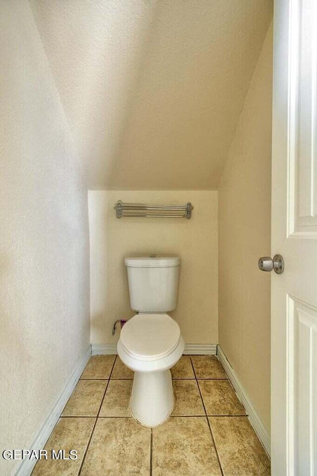 bathroom with tile floors, vaulted ceiling, and toilet