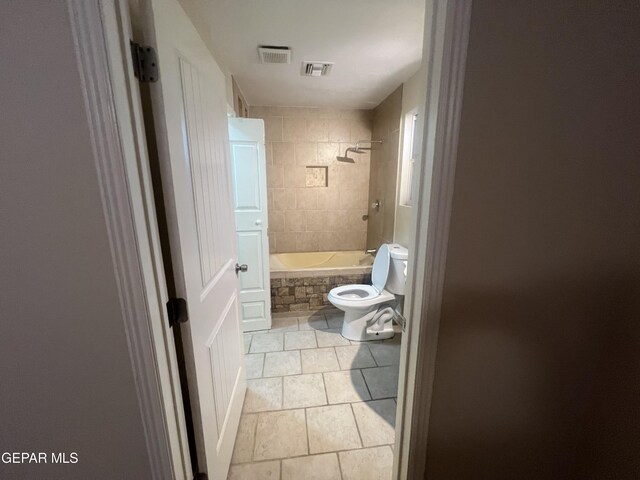 bathroom featuring tile flooring, toilet, and tiled shower / bath combo