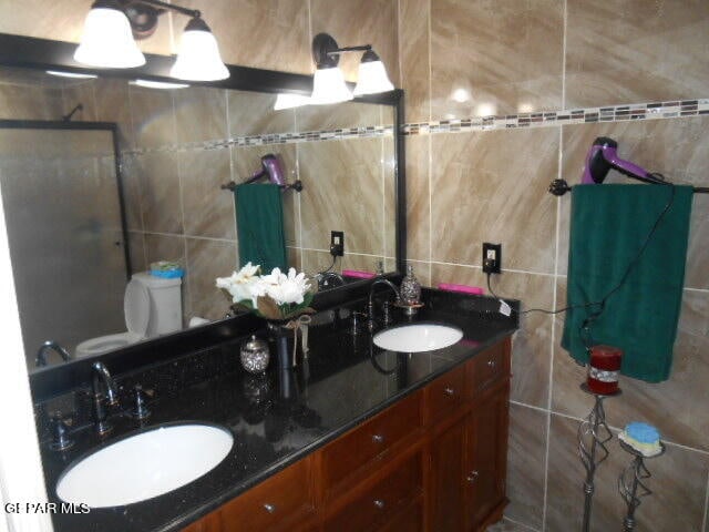 bathroom with dual sinks, oversized vanity, toilet, and tile walls