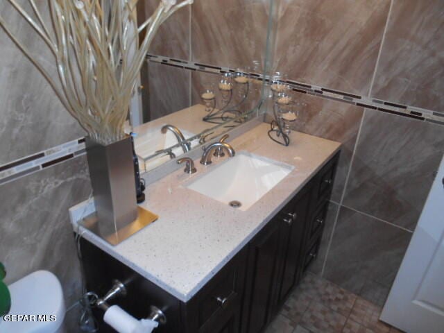 bathroom with tile floors, tile walls, toilet, and vanity