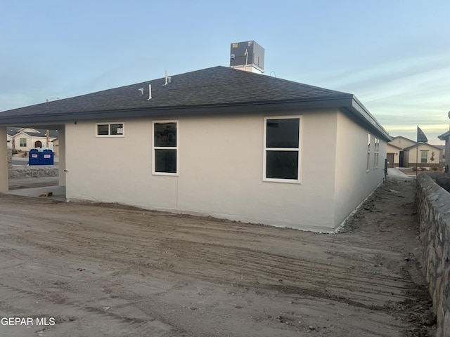 view of property exterior with stucco siding, a shingled roof, and central AC