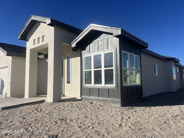 view of property exterior featuring a garage, board and batten siding, a patio area, and stucco siding