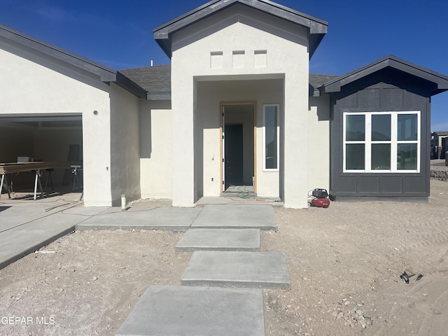 view of exterior entry featuring a garage, roof with shingles, and stucco siding