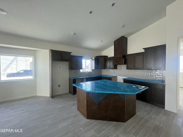 kitchen with custom exhaust hood, wood tiled floor, vaulted ceiling, and a center island