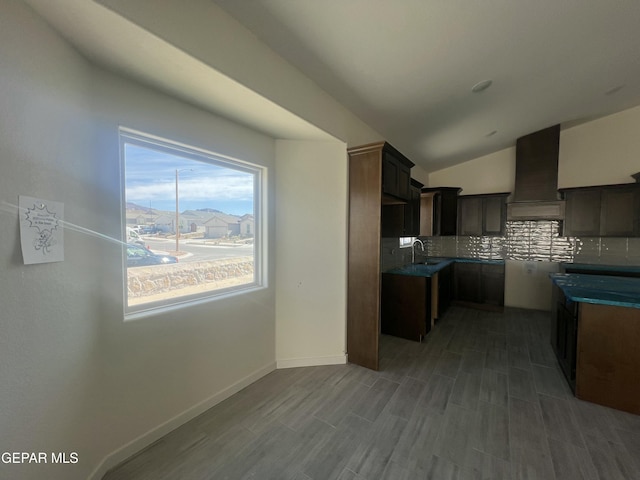 kitchen featuring baseboards, custom exhaust hood, vaulted ceiling, dark countertops, and tasteful backsplash