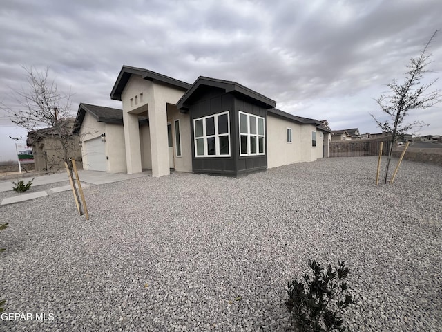 rear view of property with stucco siding, a garage, and fence