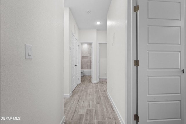 corridor with baseboards, recessed lighting, light wood-style flooring, and a textured wall