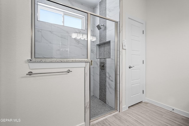 bathroom with a marble finish shower, wood finished floors, and baseboards