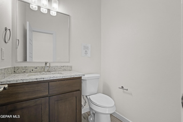 half bath featuring wood finished floors, toilet, vanity, and baseboards