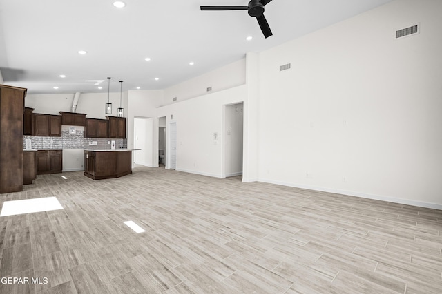 unfurnished living room with recessed lighting, light wood-style flooring, ceiling fan, visible vents, and a towering ceiling