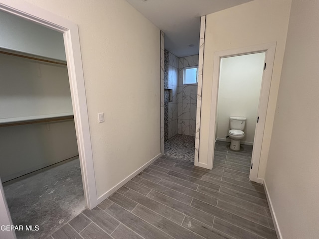 bathroom featuring a tile shower, toilet, and wood-type flooring