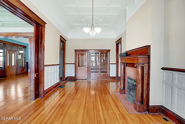 foyer entrance featuring coffered ceiling, light hardwood / wood-style floors, a fireplace, and a chandelier