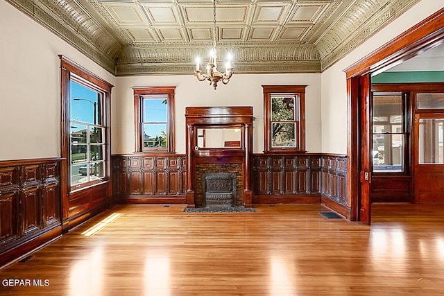 unfurnished living room with a healthy amount of sunlight, crown molding, a chandelier, and light hardwood / wood-style flooring