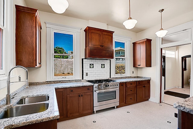 kitchen featuring light stone countertops, decorative light fixtures, backsplash, stainless steel range, and sink