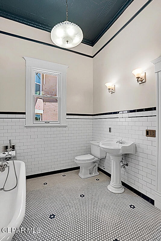 bathroom featuring tile floors, crown molding, toilet, and tile walls