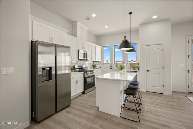 kitchen with appliances with stainless steel finishes, decorative light fixtures, white cabinetry, light hardwood / wood-style floors, and a kitchen island