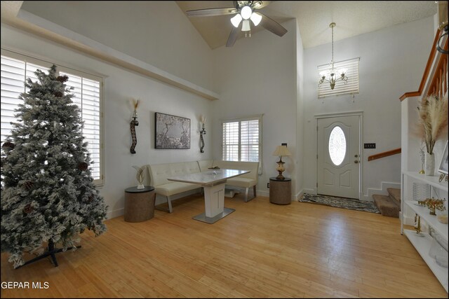 entryway featuring ceiling fan with notable chandelier, light hardwood / wood-style flooring, and a high ceiling