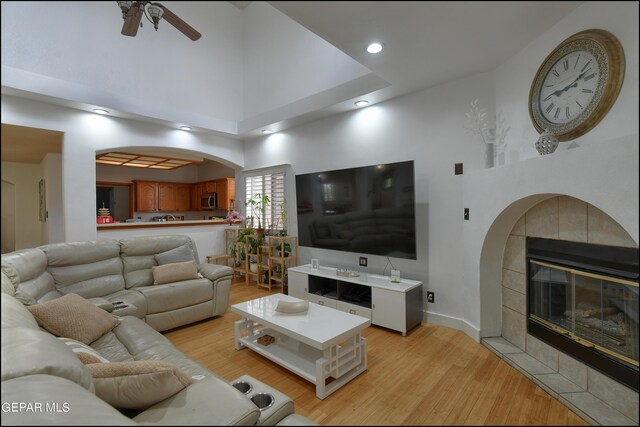 living room with light hardwood / wood-style flooring, a tile fireplace, ceiling fan, and a high ceiling