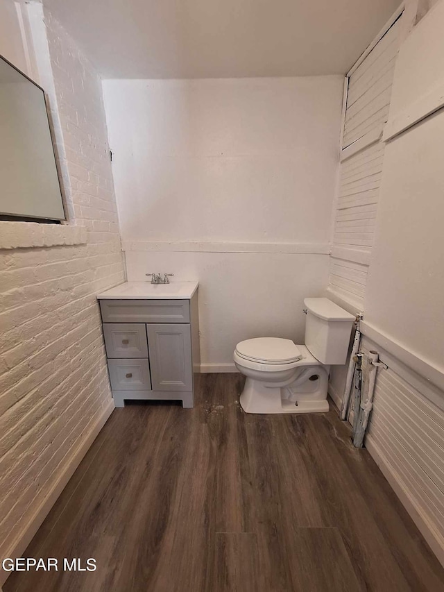 bathroom featuring brick wall, wood-type flooring, vanity, and toilet