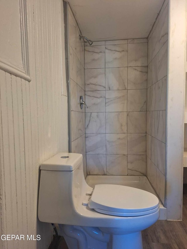 bathroom with a tile shower, toilet, and wood-type flooring