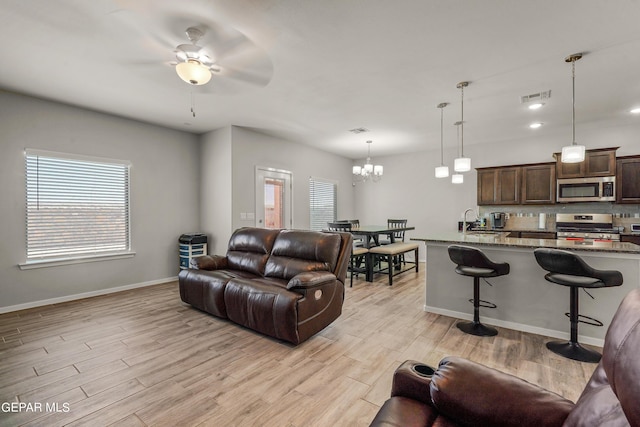 living room with ceiling fan with notable chandelier, sink, and light hardwood / wood-style flooring