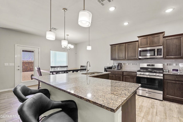 kitchen featuring sink, hanging light fixtures, stainless steel appliances, light stone counters, and backsplash