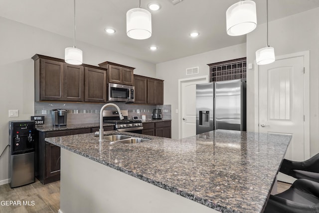 kitchen with tasteful backsplash, stainless steel appliances, hanging light fixtures, and dark stone countertops